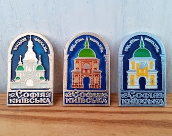 Puede incluir: Tres pines de metal plateados con esmalte azul, verde y amarillo. Cada pin presenta un detalle arquitectónico diferente de la Catedral de Santa Sofía en Kiev, Ucrania. El texto "Софія Київська" está escrito en cada pin.