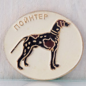 Könnte beinhalten: Eine weiße Emaille-Anstecknadel mit einer schwarzen und braunen Illustration eines Vorstehhundes. Die Anstecknadel trägt die Aufschrift "ПОИНТЕР" in goldenen Buchstaben.