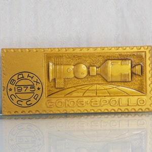 May include: A gold-colored metal plaque with a raised image of a spacecraft and the text "СОЮЗ-АПОЛЛО" (Soyuz-Apollo) and "1975".