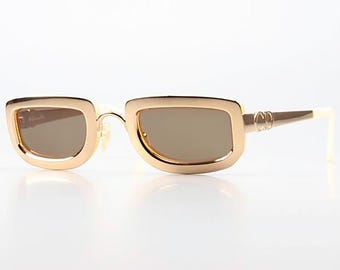 Peut inclure: Lunettes de soleil dorées avec une monture rectangulaire et des verres bruns. Les lunettes ont un logo double 'C' sur le côté.
