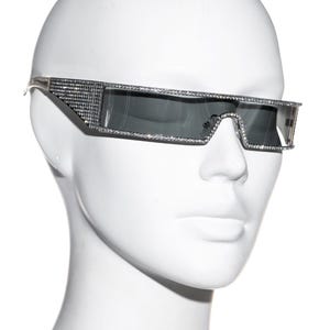 May include: A pair of black sunglasses with a silver frame and rhinestones. The sunglasses have a rectangular shape and a narrow frame.
