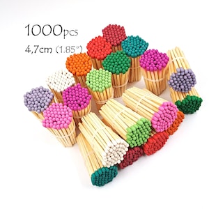May include: A collection of 1000 wooden matches, each 4.7 cm long, bundled together with small rubber bands. The match heads are dyed in various colours including red, orange, yellow, green, blue, purple, pink, and white, arranged in groups.