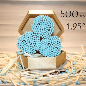 May include: A hexagonal wooden box containing three circular clusters of light blue matches, with additional loose matches scattered around the base. The text 500pcs and 1,95" is visible in the upper right corner, indicating the quantity and length.