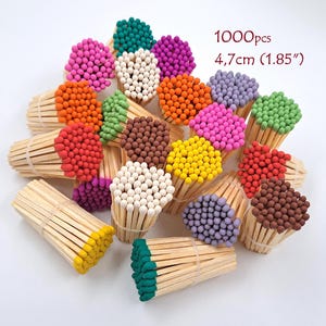 Puede incluir: Un conjunto de 1000 cerillas de madera, cada una con una longitud de 4,7 cm. Las cerillas están agrupadas en paquetes y presentan cabezas de varios colores, incluyendo rosa, naranja, verde, blanco, morado, amarillo, marrón y rojo.