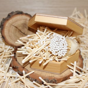 Könnte beinhalten: Eine Holzkiste gefüllt mit einem Bündel Holzstreichhölzer mit weißen Köpfen. Die Kiste ist offen und die Streichhölzer fallen heraus. Die Kiste steht auf einer Holzoberfläche.