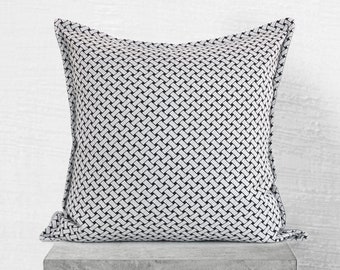 May include: A white and black woven pillow with a geometric pattern. The pillow has a square shape and is made of a soft, comfortable fabric.
