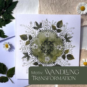 May include: Square art print featuring a central green floral design with surrounding botanical elements. The print includes the text "Motiv: WANDLUNG TRANSFORMATION" in a dark green banner at the bottom. Daisies and leaves are scattered around the print.