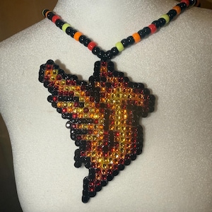 Peut inclure: Un collier avec un grand pendentif irrégulier composé de petites perles à facettes dans des tons rouge, orange et jaune, bordé de perles noires. La chaîne du collier est constituée de perles rondes alternant le noir, le rouge, l'orange et le vert citron.