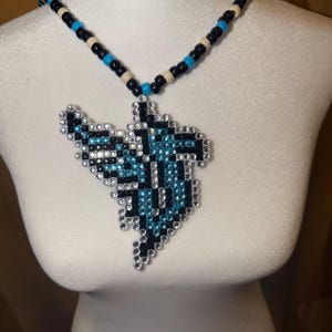 May include: A necklace featuring a large, irregular pendant crafted from small, sparkling black, light blue, and clear rhinestones. The chain is composed of alternating black, light blue, and cream-colored plastic beads strung together in a repeating pattern.