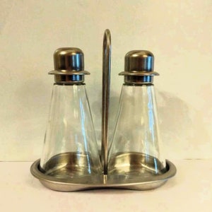 May include: A silver metal oil and vinegar dispenser set with two glass bottles and a metal stand. The bottles have silver metal lids.