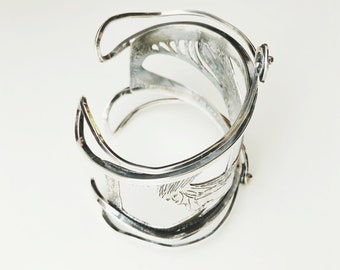 May include: Silver bracelet with an intricate design. The bracelet is open and has a hinge on one side.