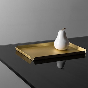 Könnte beinhalten: Ein goldfarbenes Tablett mit einer weißen Keramikbirne darauf. Das Tablett steht auf einer schwarzen Oberfläche.