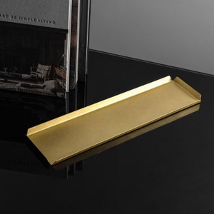 May include: A gold-colored metal tray with slightly rounded edges. The tray is sitting on a black surface.