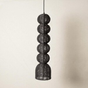 May include: A black pendant light fixture with a stacked sphere design. The light is made of woven material and hangs from a black cord. The fixture has a bulbous shape, with a series of stacked spheres, and a rounded base. The light is suspended against a neutral background.