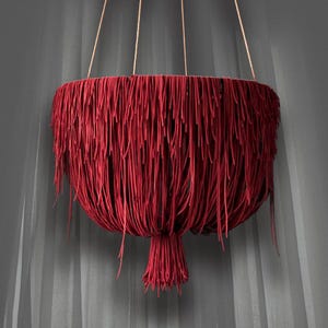 May include: A hanging red decorative light fixture. The fixture is round with long, thin, red strands hanging down, creating a fringed effect. The light is suspended by thin, light-colored cords.