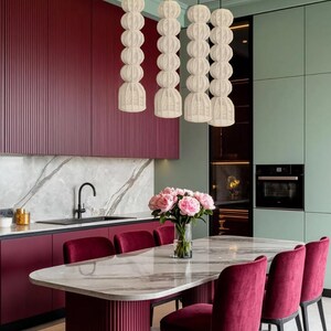 May include: A modern kitchen with a marble-topped dining table and burgundy velvet chairs. Overhead, four woven pendant lights hang above the table. The kitchen features burgundy cabinets and a mint green wall.