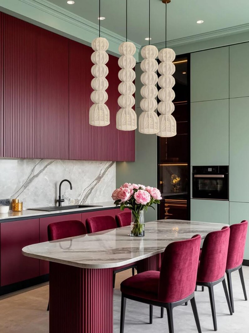 May include: A modern kitchen with a marble-topped dining table and burgundy velvet chairs. Overhead, four woven pendant lights hang above the table. The kitchen features burgundy cabinets and a mint green wall.