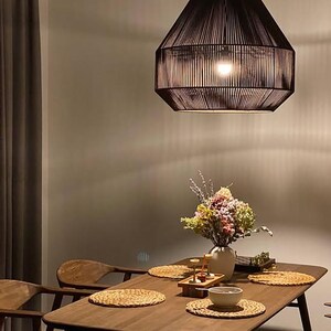 May include: A dark brown, geometric pendant light hangs above a wooden dining table. The table is set with woven placemats, a vase of flowers, and a small bowl. Wooden chairs surround the table, creating a warm and inviting dining space.