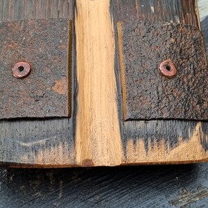 May include: Close-up of a wooden object with a central, light-colored section flanked by darker, textured panels. Copper-colored rivets secure the panels. The wood grain is visible, and the overall appearance is rustic and handcrafted.