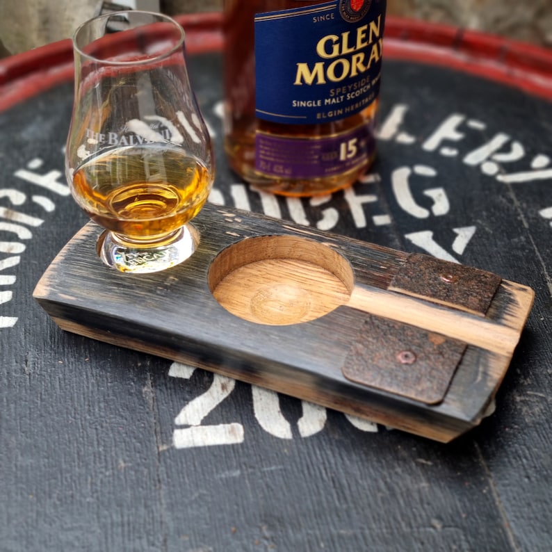 May include: A wooden whiskey flight set with a glass of amber liquid and a bottle of Glen Moray Speyside Single Malt Scotch Whisky. The set includes a round glass holder and a small rectangular holder. The wood has a dark, weathered appearance.