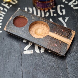 May include: A handcrafted wooden whiskey flight board with two circular cutouts and two leather accents. The board is made from reclaimed wood and has a dark, weathered finish. The board is designed to hold whiskey glasses and a small snack.