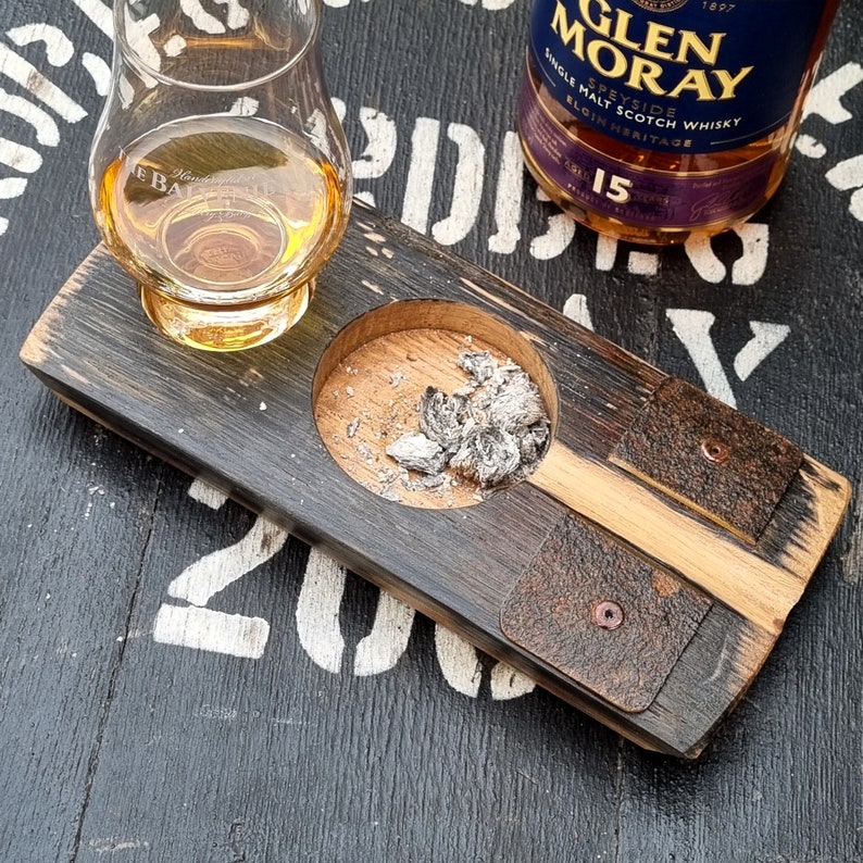May include: A wooden whiskey serving tray with a built-in ashtray and two leather accents. A glass of amber liquid sits on the tray, with a bottle of Glen Moray 15 Single Malt Scotch Whisky in the background. The tray is made from reclaimed wood.