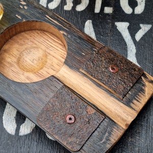 May include: A handcrafted wooden serving tray with a circular recessed area and two square coasters. The tray is made of dark and light wood, with the coasters featuring a textured, bark-like appearance and copper rivets. The tray is designed for serving drinks.