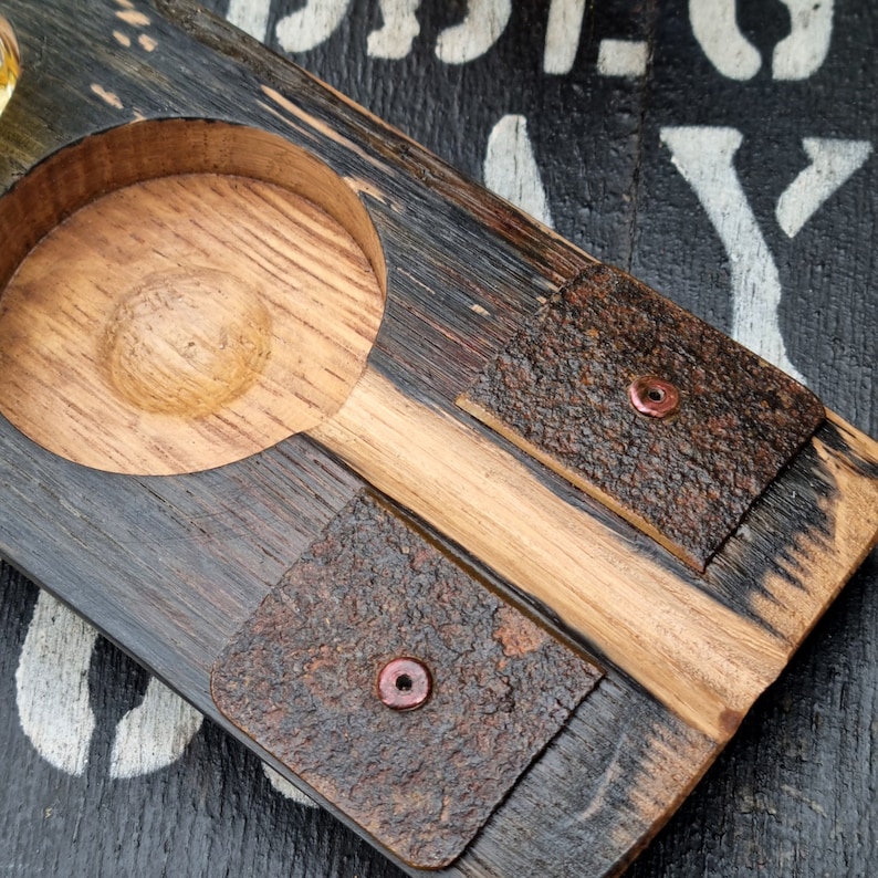 May include: A handcrafted wooden serving tray with a circular recessed area and two square coasters. The tray is made of dark and light wood, with the coasters featuring a textured, bark-like appearance and copper rivets. The tray is designed for serving drinks.