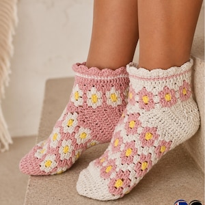 Puede incluir: Un par de calcetines de ganchillo hechos a mano en rosa, blanco y amarillo. Los calcetines presentan un patrón de margaritas y un borde festoneado. Los calcetines se muestran sobre una superficie neutra.
