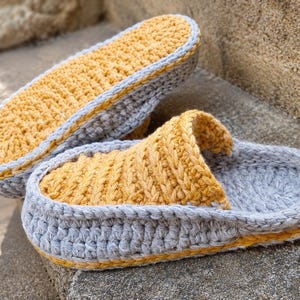 May include: Handmade crochet slippers in a cozy design. The slippers feature a gray base with a yellow interior and trim. The open-toe design is perfect for indoor wear. The slippers are made of soft yarn.