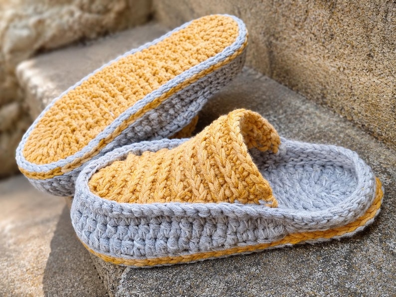 May include: Handmade crochet slippers in a cozy design. The slippers feature a gray base with a yellow interior and trim. The open-toe design is perfect for indoor wear. The slippers are made of soft yarn.