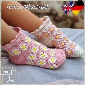 May include: Crocheted socks in pink and white with yellow flower accents. The socks have a scalloped edge and are shown on a person's feet. The image includes the text "HÄKELANLEITUNG" and a PDF icon.