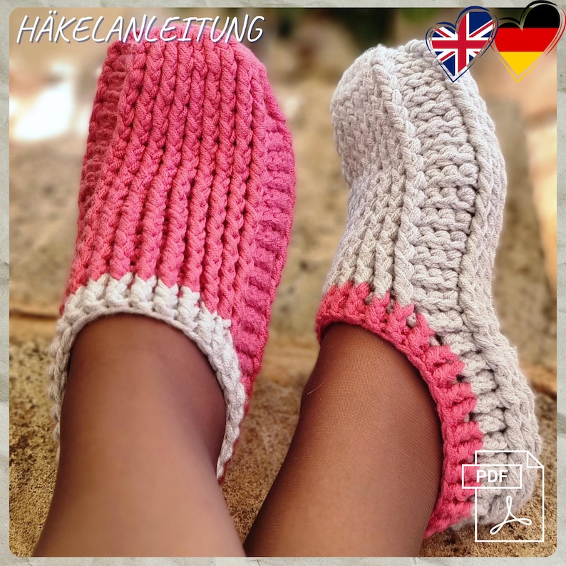 May include: A pair of handmade crochet slippers in pink and gray. The slippers have a ribbed texture and a white trim on the pink slipper. The text "H&Auml;KELANLEITUNG" is visible at the top of the image.