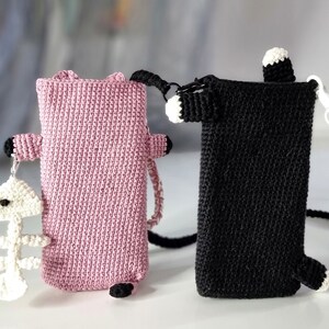 Op de afbeelding: Twee gehaakte telefoonhoesjes in de vorm van een kat. E&eacute;n is roze met zwarte accenten en een witte visgraatbedel. De andere is zwart met witte accenten en een zwarte koordriem. Beide hebben een rechthoekig ontwerp.