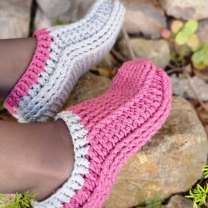 May include: A pair of handmade crochet slippers in shades of pink and gray. The slippers have a thick, textured stitch pattern and a contrasting color trim. The cozy footwear is perfect for indoor wear.