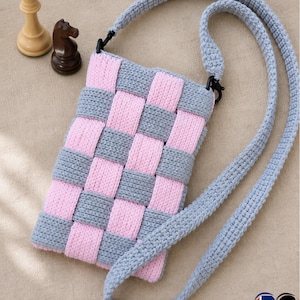 May include: A handmade, woven-style crossbody bag in pink and gray. The bag features a checkerboard pattern and a long, gray strap. Two chess pieces, a queen and a knight, are visible in the background.