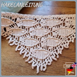 Puede incluir: Primer plano de un ribete de encaje de ganchillo beige con un borde festoneado. El encaje presenta un diseño calado con formas ovaladas repetidas y el texto "HAKELANLEITUNG" en la parte superior. Un icono PDF con banderas inglesa y alemana está en la esquina inferior derecha.