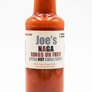 May include: A glass bottle of Joe's Naga Rings on Fire! Extra Hot Chilli Sauce. The bottle is filled with a red sauce and has a black cap. The label is white with black text.