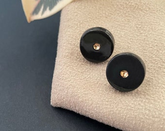 May include: A pair of black ceramic earrings with a gold dot in the center of each earring.