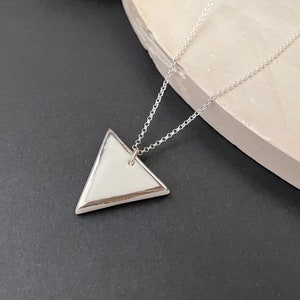 May include: A silver chain necklace with a white ceramic triangle pendant.