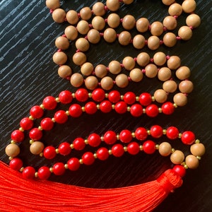 May include: Two strands of beaded necklaces, one with red beads and one with brown beads. The red beaded necklace has a red tassel.