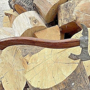 May include: A hand-forged axe with a wooden handle and a patterned steel blade. The axe is resting on a pile of logs.