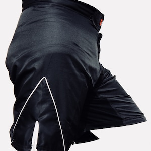 K&ouml;nnte beinhalten: Schwarze Sport-Shorts mit wei&szlig;em Besatz und einem kleinen orangen Logo am Bund.