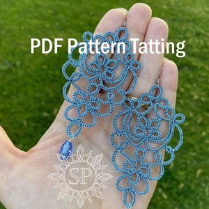 Può includere: Un paio di orecchini in pizzo blu con perline di cristallo blu che pendono dalla parte inferiore. Gli orecchini sono tenuti in una mano con il testo "PDF Pattern Tatting" e "TATFANTASY Silvia Passaquieti" visibile.
