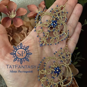 Può includere: Orecchini in perle dorate e blu con un design delicato e intricato. Gli orecchini sono fatti a mano e presentano un piccolo cristallo blu al centro di ogni orecchino. Gli orecchini sono etichettati "TATFANTASY Silvia Passaquieti".