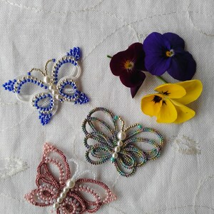 May include: Three beaded butterfly brooches in blue, pink, and green with white accents. Each brooch has a pearl in the center.