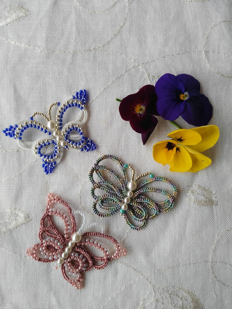 May include: Three beaded butterfly brooches in blue, pink, and green with white accents. Each brooch has a pearl in the center.