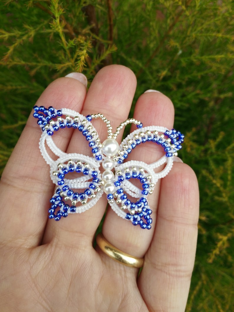 May include: A white and blue beaded butterfly brooch with a pearl accent. The butterfly is made with small seed beads and has a delicate, intricate design.