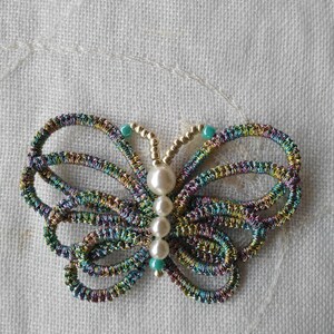 May include: A colorful butterfly brooch made of woven thread with a pearl and turquoise bead accents.