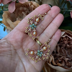 Può includere: Un paio di orecchini dorati con un delicato design a farfalla. Gli orecchini sono realizzati con perline rosa e verdi e presentano un accento di perla.